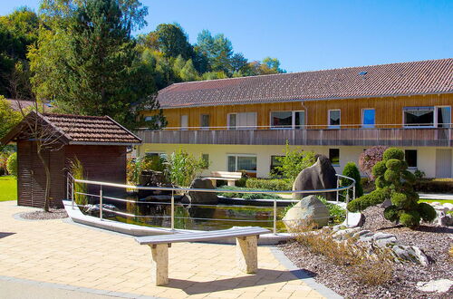 Garten mit Teich, Brücke und bepflanzten Steinen vor einem zweistöckigen Gebäude mit gelber Fassade und braunem Dach