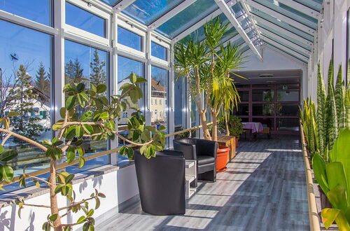 Wintergarten mit großen Fenstern, mehreren Pflanzen und zwei schwarzen Sesseln