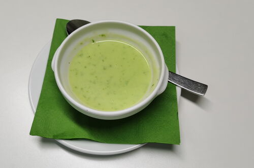 Schüssel mit grüner Bärlauch Suppe auf grünem Serviettenpapier auf weißem Teller mit Löffel