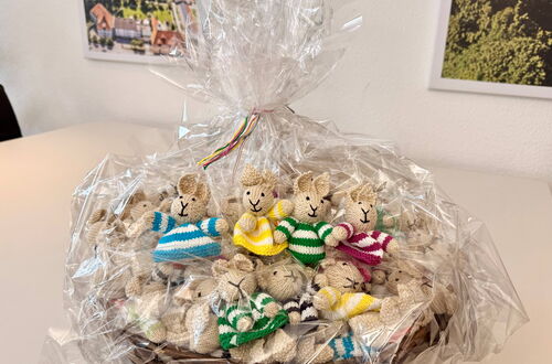 Korb mit mehreren kleinen gestrickten Hasenfiguren in bunten gestreiften Pullovern, verpackt in durchsichtige Folie