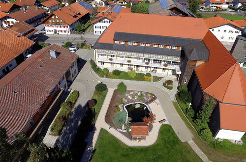 Luftaufnahme eines Gebäudekomplexes mit roten Dächern, einem Innenhof mit Teich und umlaufenden Wegen