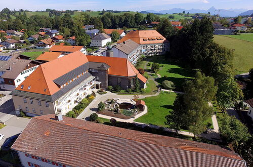Luftaufnahme vom Pflegeheim mit roten Dächern, umgeben von Bäumen und Wiesen, im Hintergrund Berge