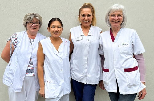Vier Frauen in weißen medizinischen Kitteln stehen vor einer hellen Wand
