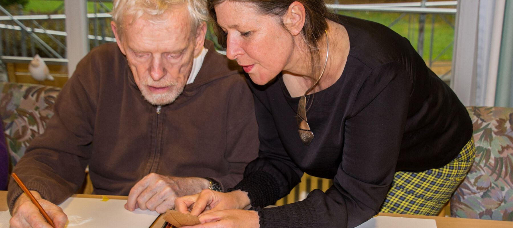 Zwei Personen sitzen an einem Tisch und zeichnen mit Buntstiften auf Papier