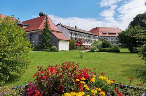 Blumenbeet mit roten und gelben Blumen vor einem großen Gebäude mit roten Dächern und einer kleinen Kirche mit Zwiebelturm im Hintergrund
