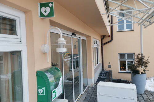 Außenwand eines Gebäudes mit grünem Defibrillatorkasten und grünem Schild mit Herzsymbol über dem Kasten