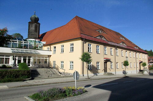 Großes gelbes Gebäude mit rotem Satteldach und kleinem Turm mit Zwiebelhaube neben einer Straße