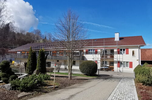 Zweistöckiges Wohnhaus mit roten Fensterläden, Gerüst an der Fassade, davor Baum und gepflegte Gartenanlage mit Weg