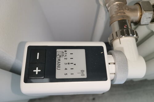 Heizkörperthermostat mit digitaler Anzeige und Plus- und Minus-Tasten an einem Heizungsrohr