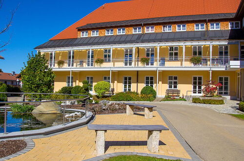 Gelbes mehrstöckiges Gebäude mit Balkonen vor einem Teich und Sitzbank auf gepflastertem Weg