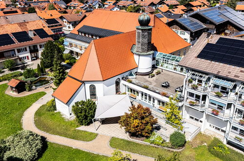 Luftaufnahme eines Gebäudekomplexes mit einem Kirchenschiff mit rotem Satteldach und einem angrenzenden modernen Flachbau mit Solarpaneelen auf dem Dach