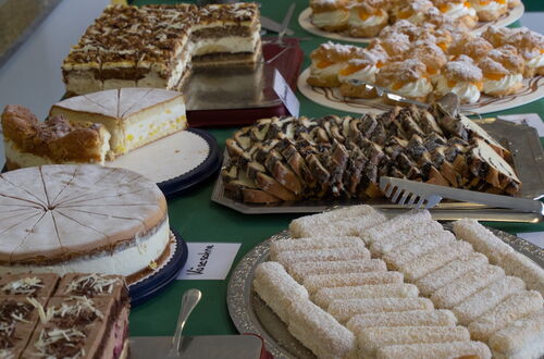 Verschiedene Kuchen und Gebäckstücke auf Tellern und Tabletts auf einem grünen Tisch verteilt